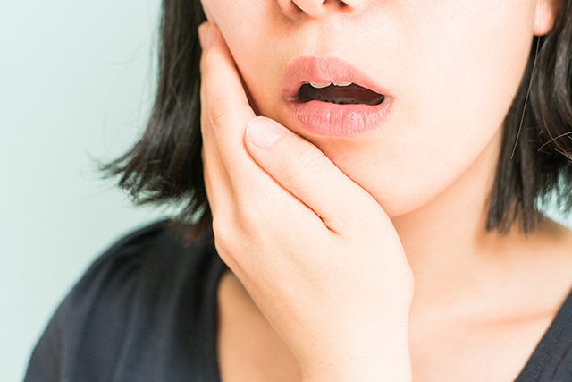 歯茎に違和感を感じ頬に手を当てる女性